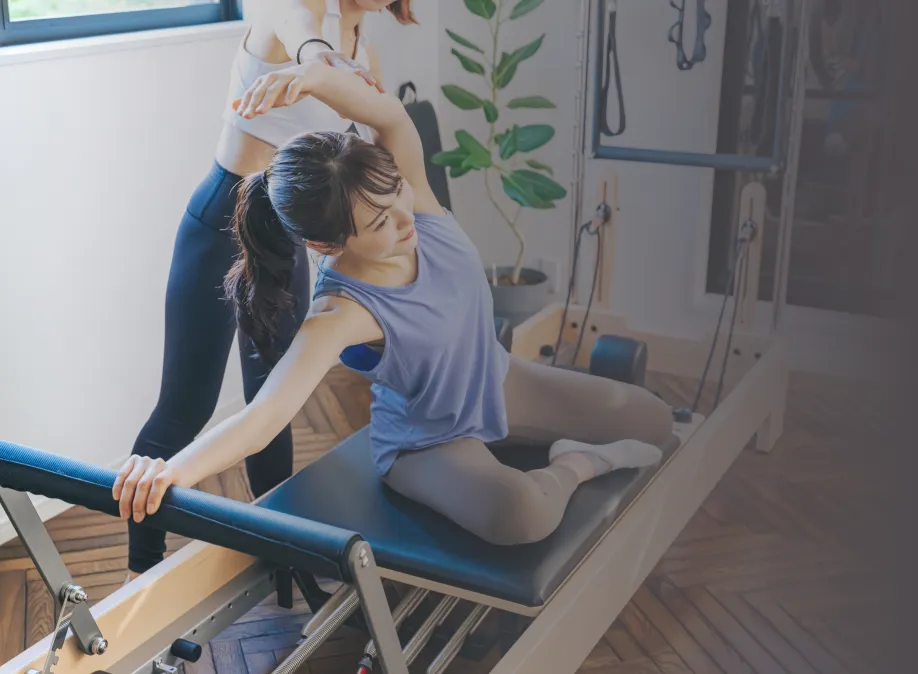 女性とトレーナーがピラティスをする様子